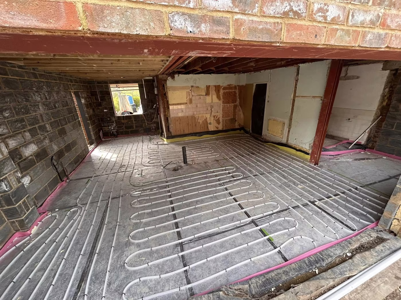 Underfloor heating pipe laid in loops across insulation boards in a brick extension
